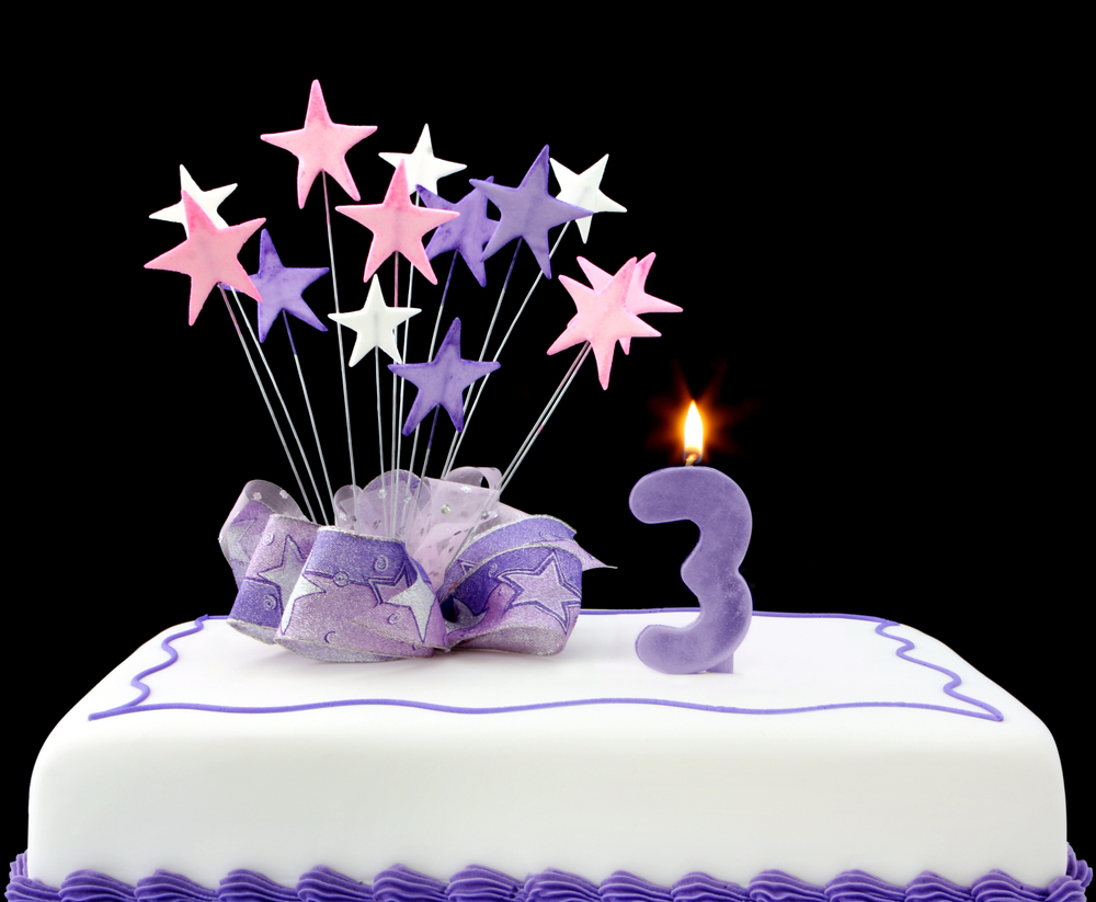 birthday cake with purple stars and a lit purple candle in the shape of a 3 on top